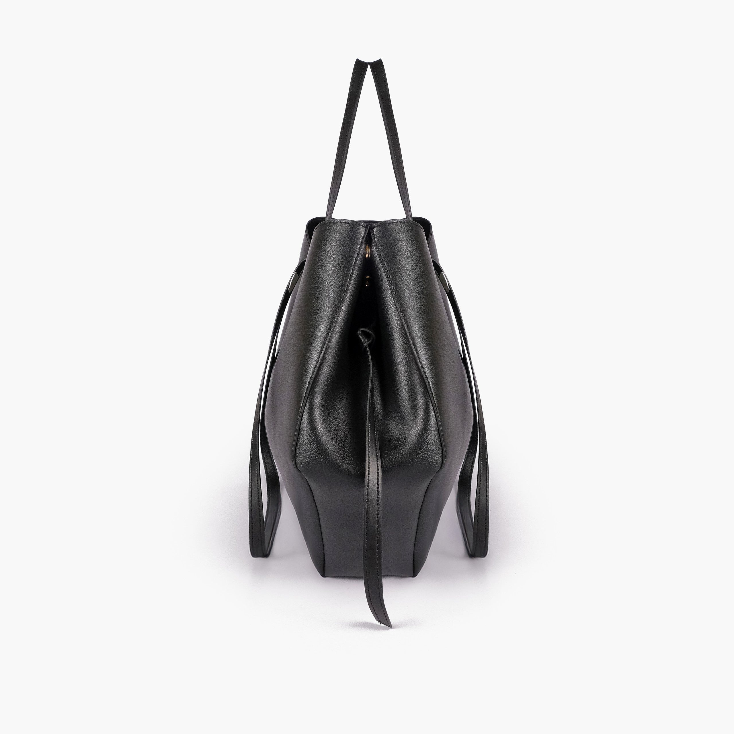 Black atelier tote — side profile showing wing-cut origami fold, cinch tie, and slim shoulder handle