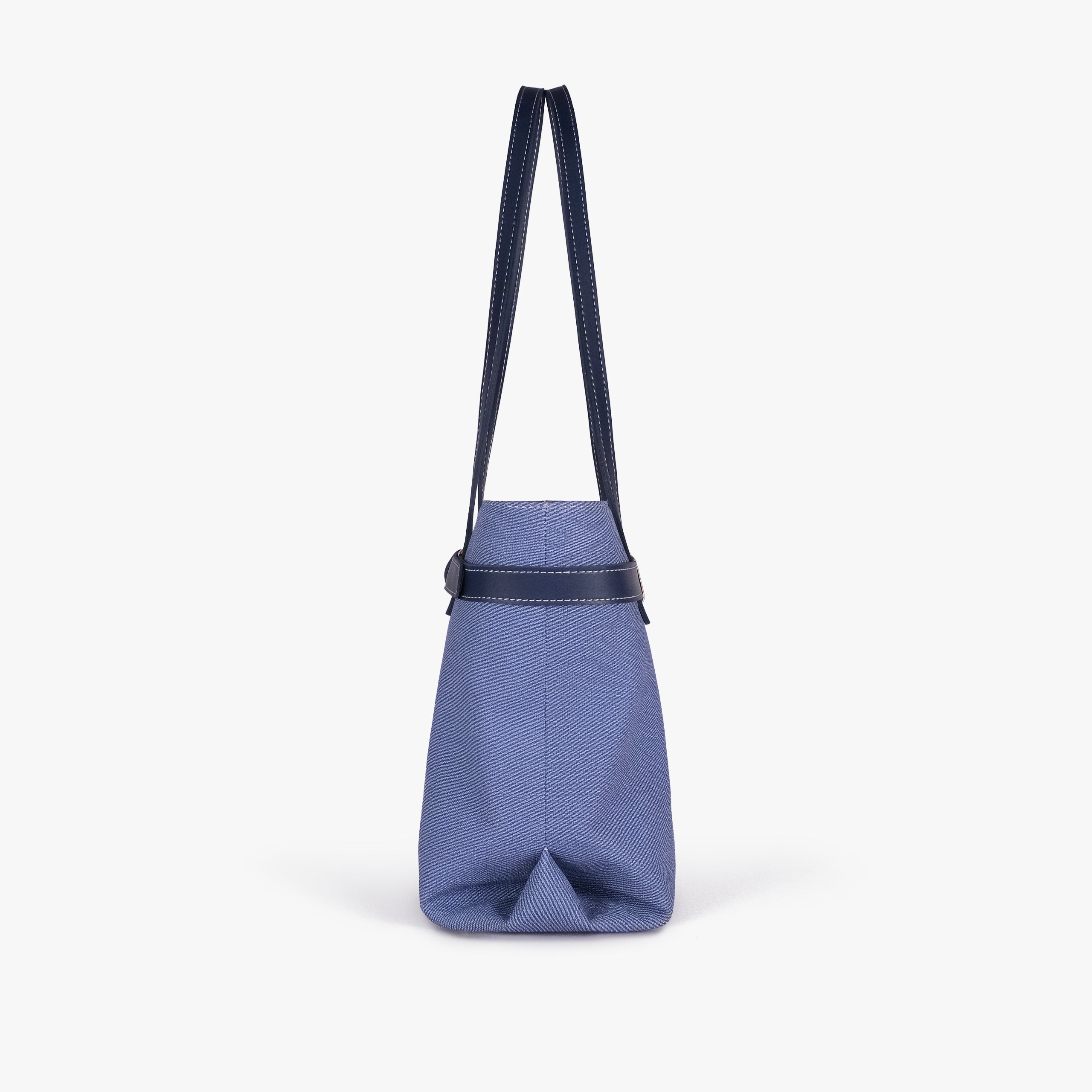 Navy belted tote bag — side profile showing the slim depth, folded side gusset, smooth trim edge, and long shoulder handle drop, blue-navy textured body with dark smooth faux-leather trim